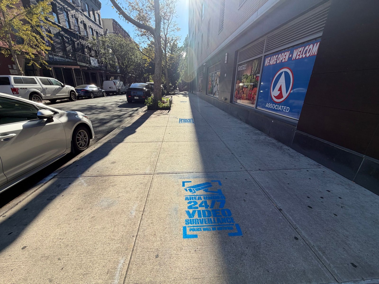Blue camera and surveillance-awareness sidewalk stencil in Harlem