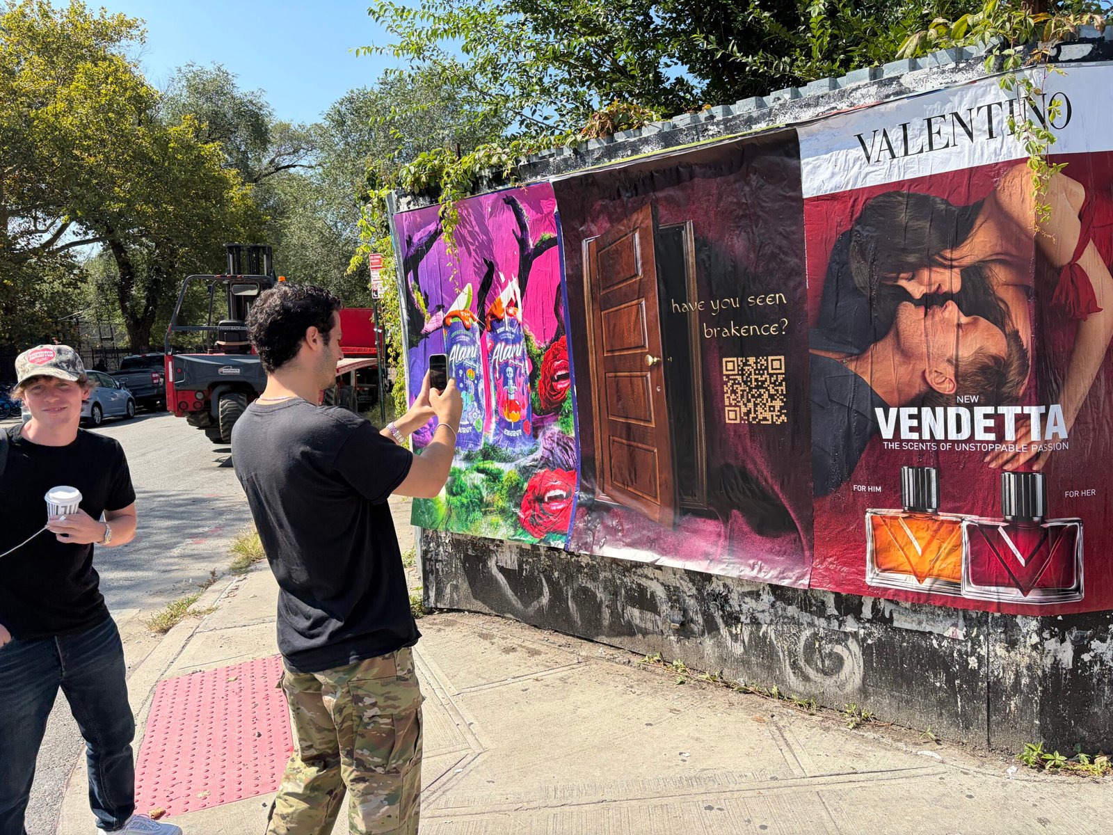 Person photographing QR-code artwork beside a large-format street poster display