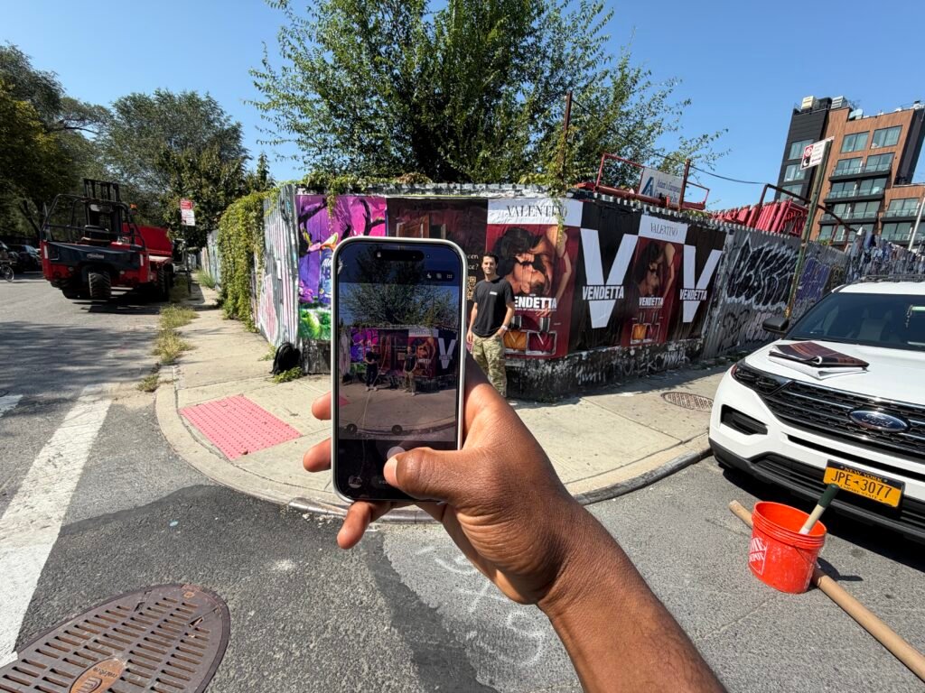 Phone photographing a street poster display with QR-code and Valentino artwork
