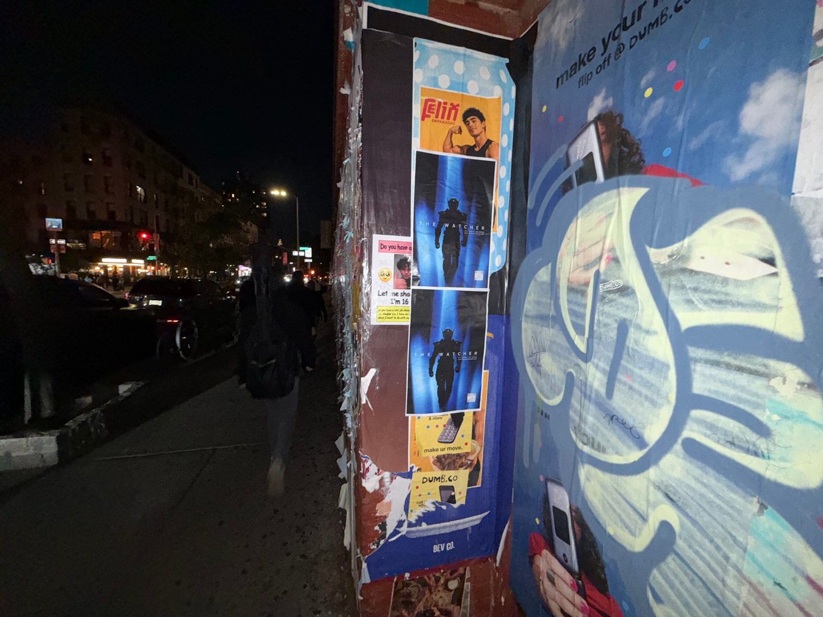 Two The Watcher posters stacked beside a graffiti-covered storefront shutter.